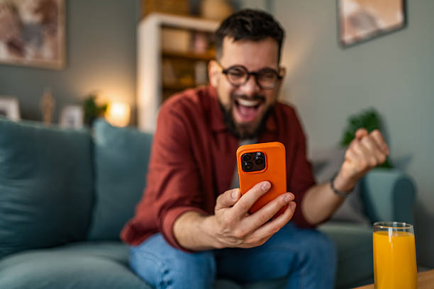 Excited young man using smart phone at home and celebrating.