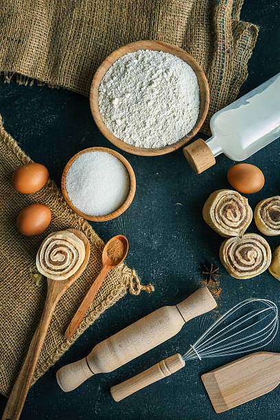 istock A top-down view of cinnamon buns on a dark surface with flour, sugar, eggs, milk, and a rolling pin, perfect for baking and recipe themes. 2208416343