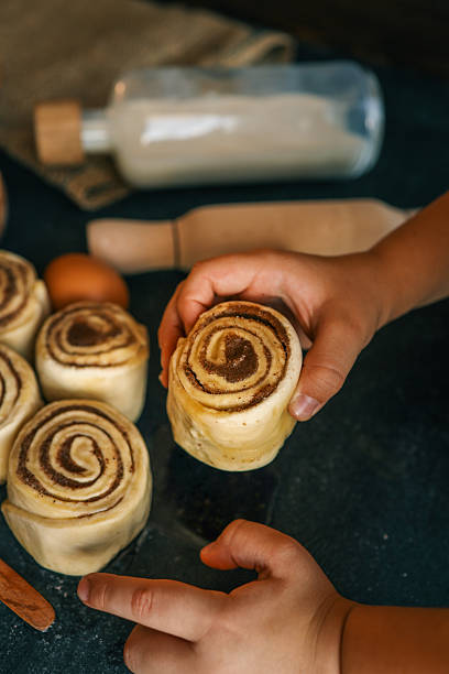 istock Children rolling cinnamon buns on a dark surface with flour, sugar, eggs, and milk, capturing a cozy baking scene, perfect for family cooking themes 2208416353