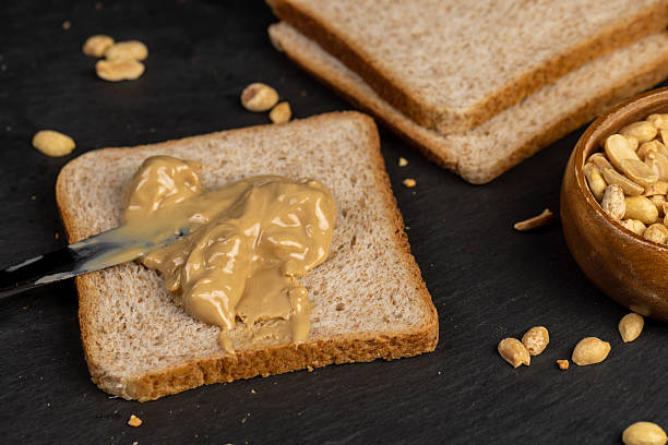 istock peanut butter on a piece of bread and roasted peanuts on the table 2208419990