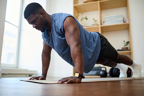 African American man wearing athletic clothing performing push-ups on an exercise mat indoors, concentrating on workout