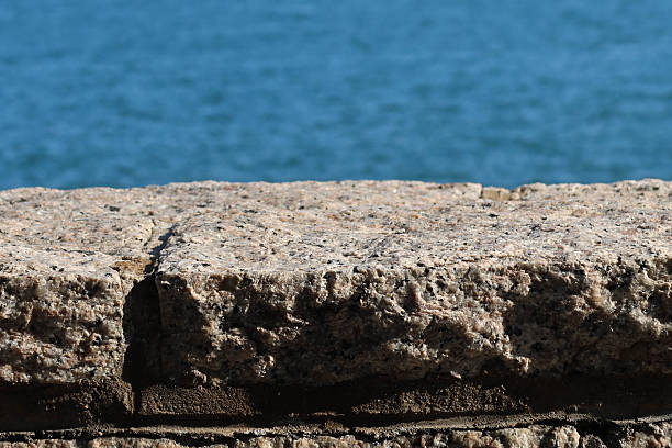 istock A textured imperfect stone granite ledge with rugged surface. A serene blue hue sea at the back. 2208423665