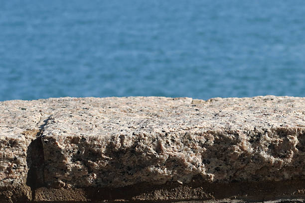 istock A textured imperfect stone granite ledge with rugged surface. A serene blue hue sea at the back. 2208423666