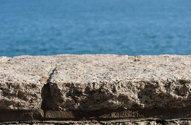 istock A textured imperfect stone granite ledge with rugged surface. A serene blue hue sea at the back. 2208423668