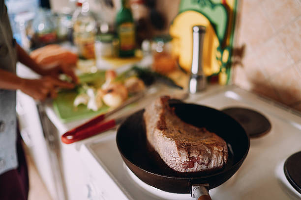 Roast beef is stewed in a pan while the chef cuts vegetables on the table. Cropped. High quality photo