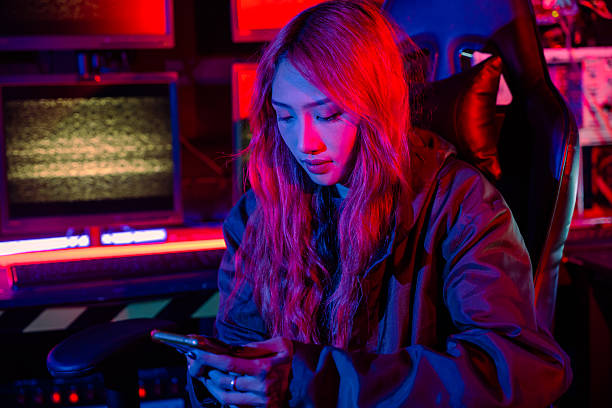 istock Woman hacker. Asian woman wearing hood working at computer and mobile phone typing coding hacking programming system. Hacker browsing internet uses malware with smartphone to hack password 2208427357