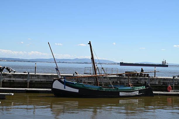 Lisbon, Portugal, march 25, 2025 : Old sailing ship moored in a Lisbon port with a cargo ship sailing on the Tagus River in the background