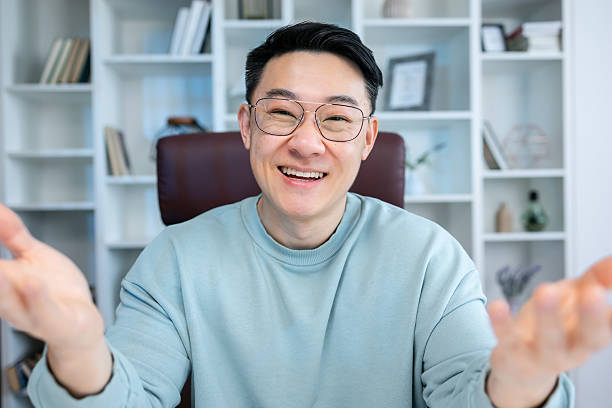 istock Friendly happy young asian man waving hand saying hello looking at camera greeting distant friend making online call, cheerful male vlogger blogger recording vlog teaching e-coaching via webcam 2208429001