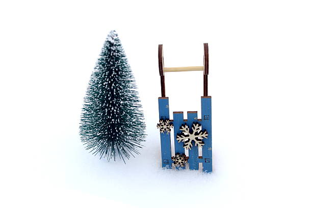 On a white background in the snow there is a toy sleigh with a Christmas tree.