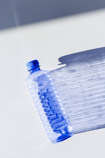 istock Transparent plastic bottles with blue caps and sun shadows on light background. Top view Water bottles at natural light. Themes of recycling, sustainability, water conservation, minimal style 2208431131