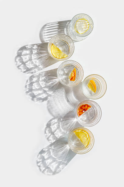 istock Crystal glasses with citrus slices in water on white background with reflections at sunlight, modern, minimalist composition with clear glass cups filled with water and citrus fruit, as lemon, orange 2208431664