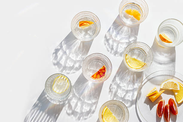 istock Fruit Infused Water in transparent Glasses with Shadows at sunlight on White background. Aesthetic view summer healthy drink with slices of lemon, orange with rainbow sun glare from glass cups, above 2208431665