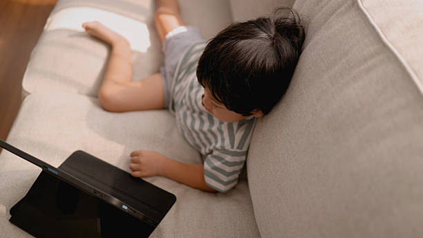 istock Asian little boy using tablet on sofa watch cartoon , playing game. 2208433119