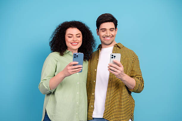 istock Smiling young couple using smartphones together against a bright blue background, capturing happy moments and bonding digitally 2208434861