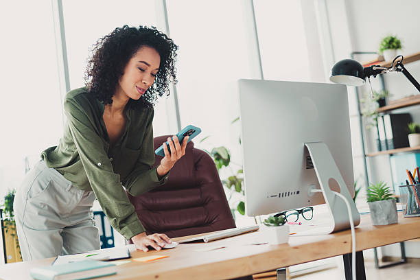 istock Young businesswoman looking at her phone while working at a trendy workspace with modern office decor and bright natural daylight 2208436202