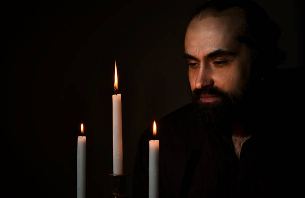 istock Man Contemplating by Candlelight in Dark Room 2208436384
