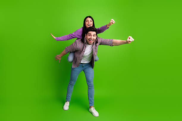 istock Couple having fun together performing a playful flying pose against a vibrant green background, embracing joy and shared moments 2208436587