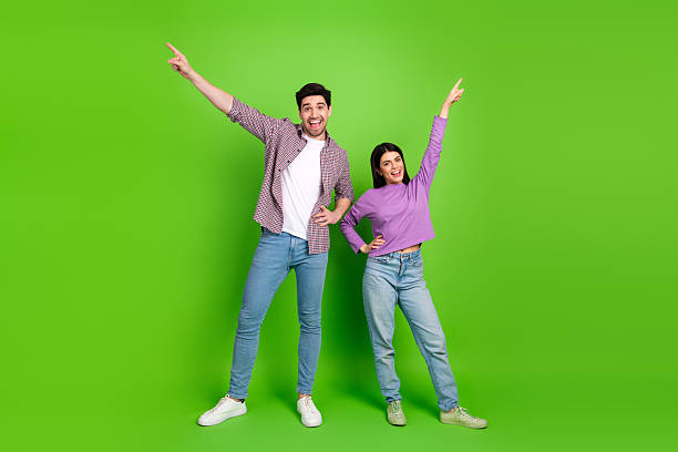 istock Young couple striking playful poses pointing upward on a green background, showcasing joy, friendship, and a fun casual lifestyle 2208436633