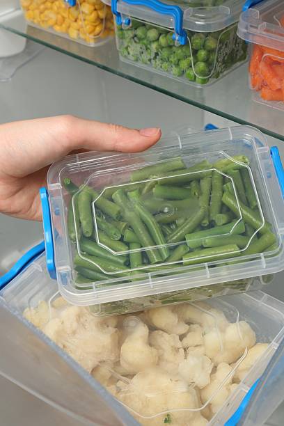istock Woman taking plastic container with frozen green beans from refrigerator, closeup 2208437225