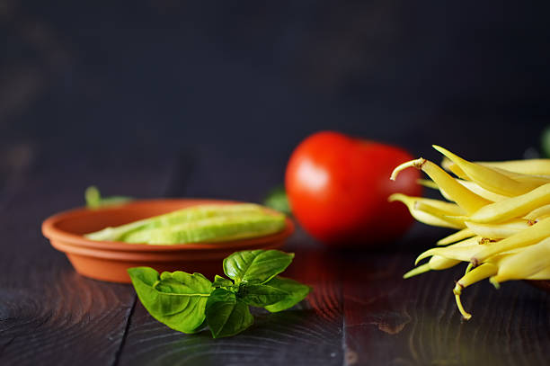 Juicy tomato, crispy asparagus, and aromatic basil lie next to tender zucchini rings, harmoniously arranged on the plate. The bright colors of the vegetables contrast with the dark background, emphasizing their freshness. Kitchen still life.
