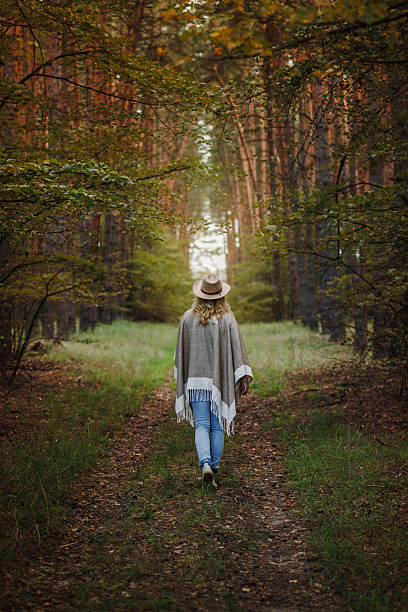 istock Woman wearing poncho and cowboy hat walks on forest footpath 2208438546