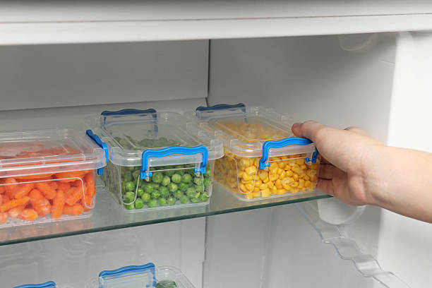 istock Woman taking plastic container with frozen corn from refrigerator, closeup 2208440163