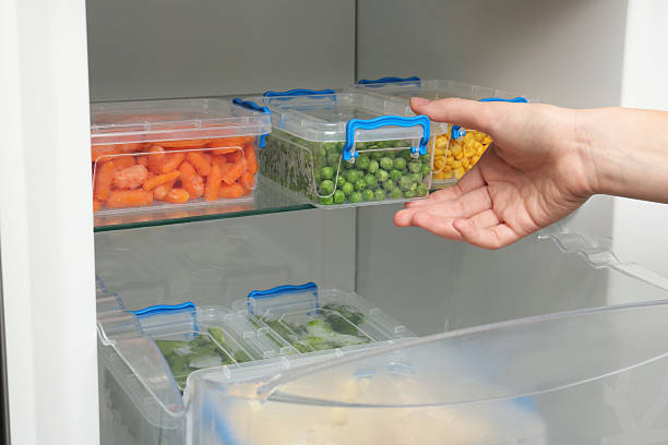istock Woman taking plastic container with frozen green peas from refrigerator, closeup 2208440173