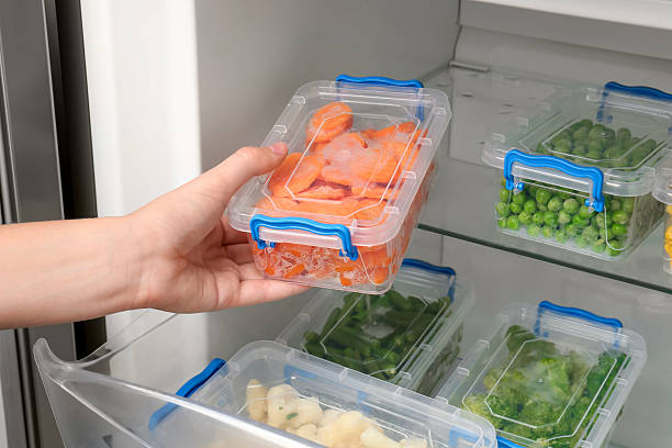 istock Woman taking plastic container with frozen carrot from refrigerator, closeup 2208440174