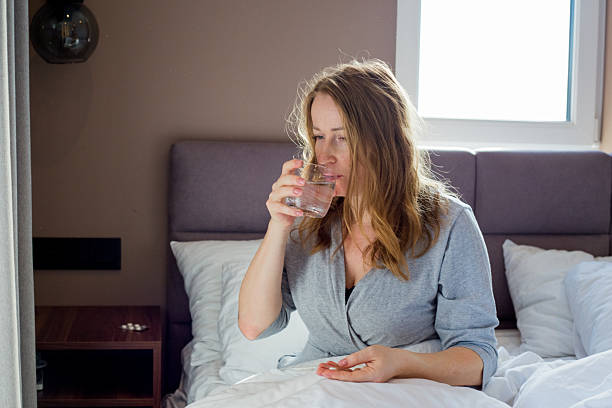 istock Woman taking medication and drinking water in bed 2208442241