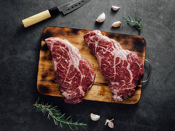 istock Raw marbled beef cuts on wooden board with herbs and garlic on dark stone surface 2208443859