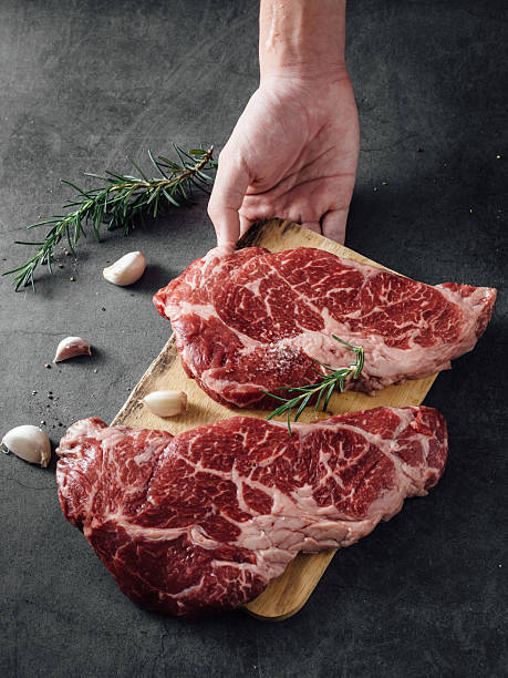 Fresh Raw Beef Cuts on Wooden Board with Garlic and Rosemary Garnish in Kitchen Setting