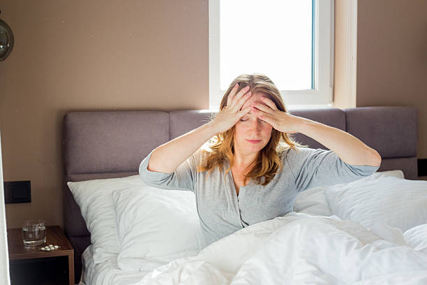 istock Woman with headache sitting in bed holding head 2208444186