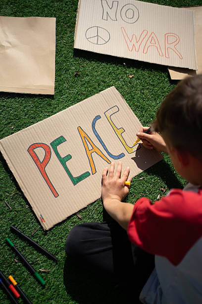 istock Young boy drawing peace signs on cardboard, sitting on grass 2208445573