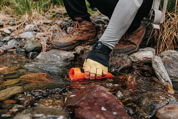 istock Young hiker fills bottle with clear water from serene forest stream 2208446670