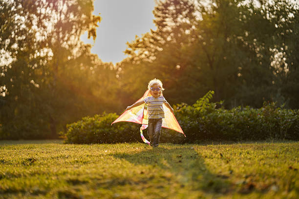 istock Boy pretends to fly while playing with a kite in the park 2208450276