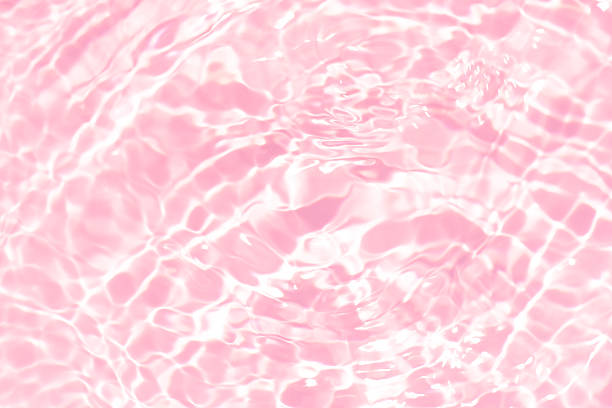 Pink water bubbles on the surface ripples. Defocus blurred transparent pink colored clear calm water surface texture with splash and bubbles. Water waves with shining pattern texture background