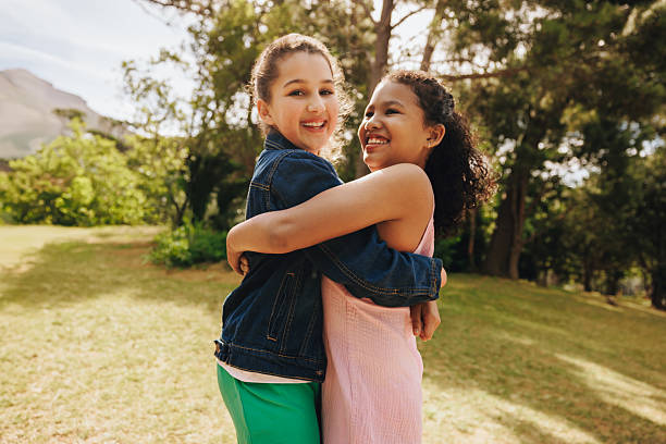 istock Two smiling friends hugging outdoors in a sunny park setting 2208451258