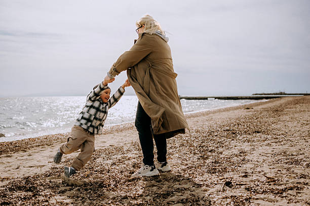 istock Joyful mom spinning her child on the beach during autumn 2208453490