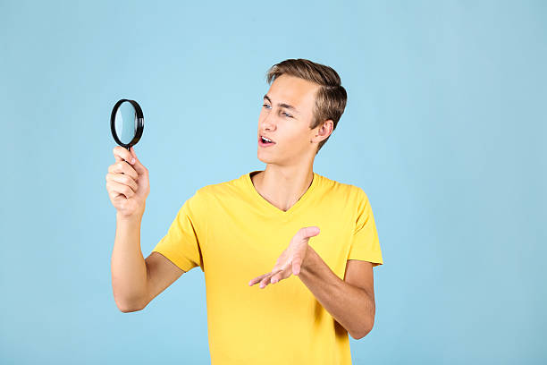istock Young man with magnifying glass on blue background 2208455385