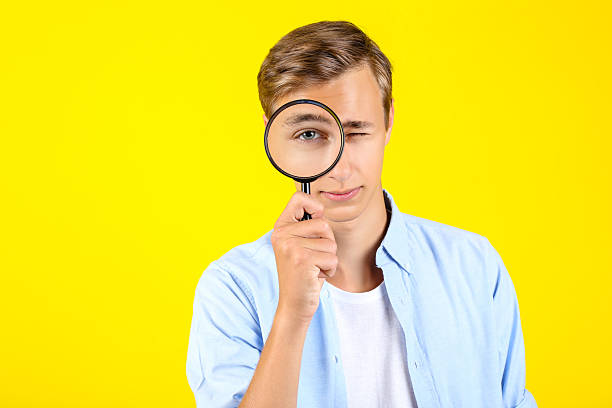 istock Young man with magnifying glass on yellow background 2208456095