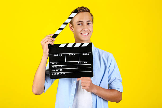 istock Young man with clapper board on yellow background 2208456219