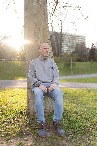 istock Bald man relaxing under tree in urban park at sunset 2208458073