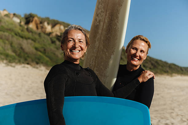 istock Two smiling friends holding their surfboards on the beach before surfing 2208459671