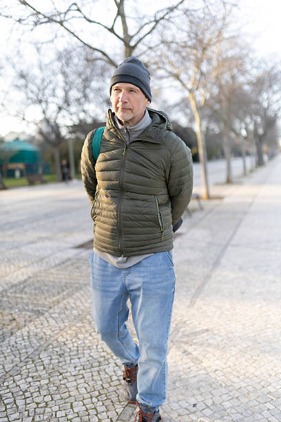 istock Senior man walking in park wearing winter clothes and backpack 2208460412