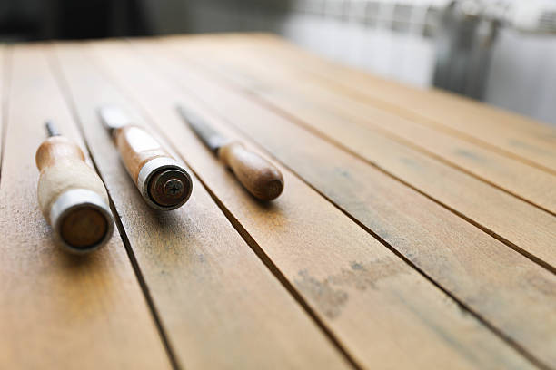 A close-up of vintage metal files with wooden handles on a rustic workbench. The focus is on the foreground file, highlighting its textured surface and worn grip, while the others fade into the background.