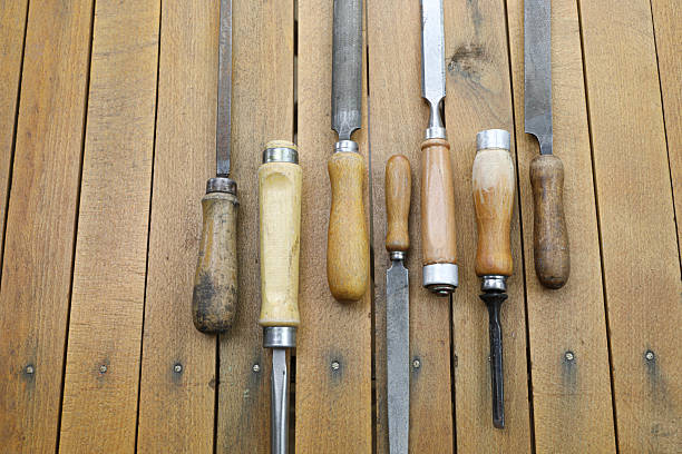 A close-up of vintage metal files with wooden handles on a rustic workbench. The focus is on the foreground file, highlighting its textured surface and worn grip, while the others fade into the background.