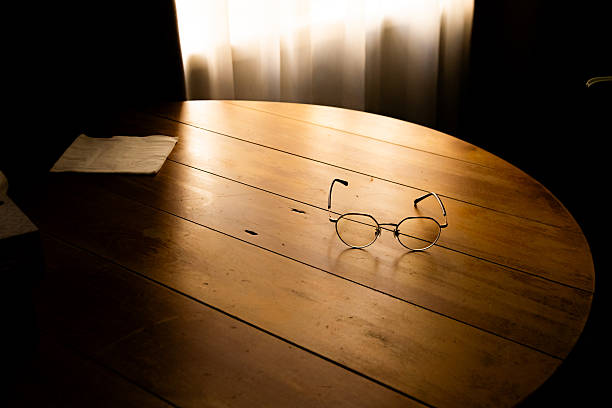 Eyeglasses are put on a wooden table while sunlight is cast via a white curtain.