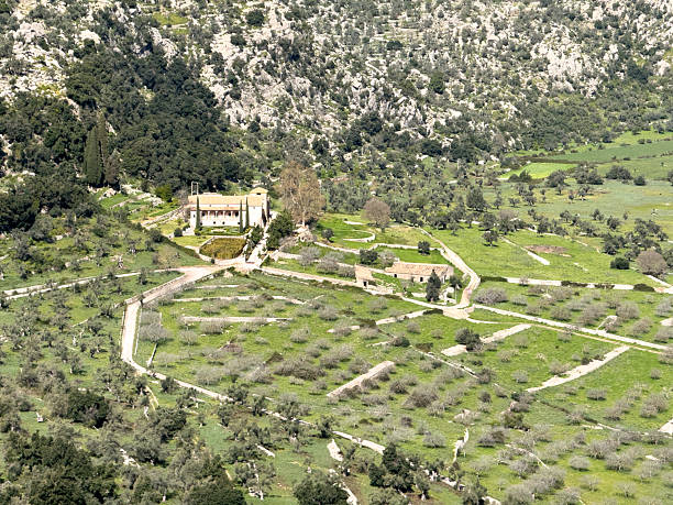 A picturesque view of a Mediterranean village in Majorca, Spain, showcasing stone-built houses amidst lush greenery and rolling hills.