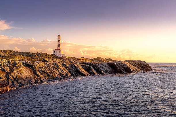 Faro de Favaritx Golden Hour. Menorca Striking Lighthouse Amidst a Sunset Glow. A breathtaking sunset over the iconic lighthouse and its rocky surroundings