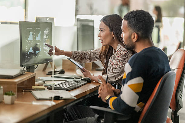 Mixed Race Businessman and Asian Businesswoman Analyzing Data on Office Computer in Bright Workspace